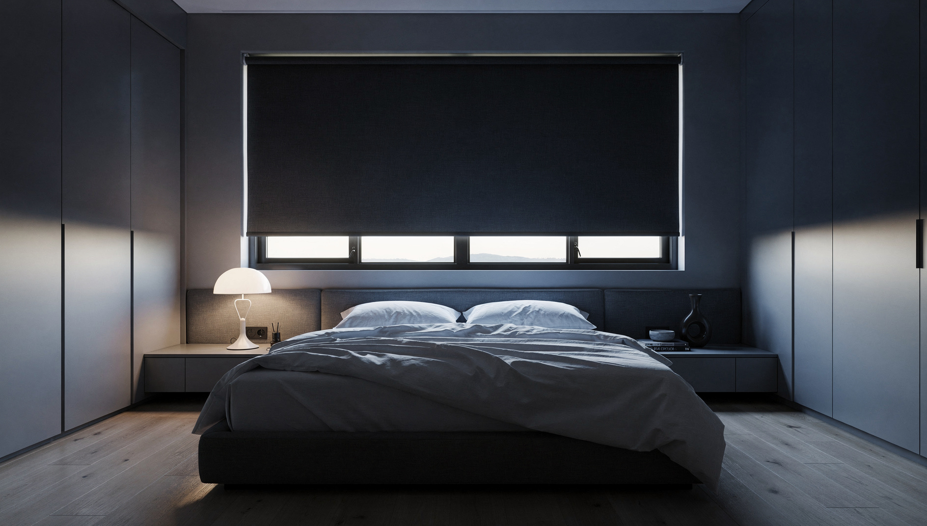 Charcoal blockout roller blind lowered over a wide bedroom window with a thin sliver of daylight at the bottom
