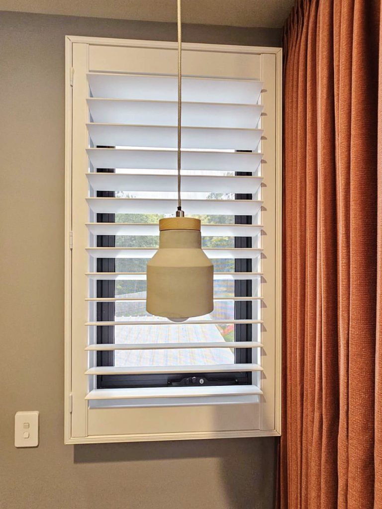 Orange pinch pleat curtains complemented by white shutters.