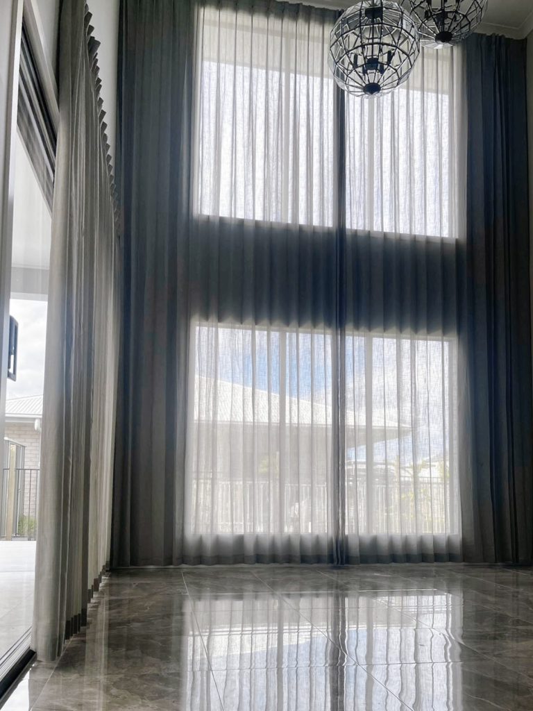 Grey pinch pleat sheers elegantly draping a tall window in a living room.